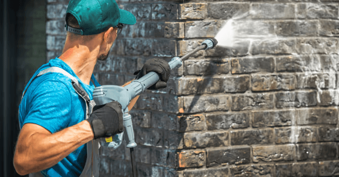 Nettoyage à haute pression d’un mur extérieur en briques foncées par un travailleur utilisant une laveuse à pression.