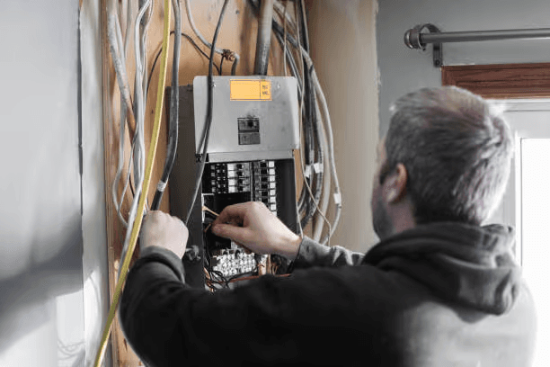 Électricien effectuant des travaux de câblage dans un panneau électrique résidentiel ouvert, avec disjoncteurs et fils visibles
