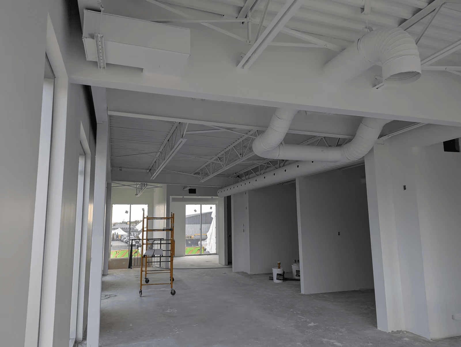Local commercial en rénovation intérieure avec plafond ouvert peint en blanc, conduits de ventilation apparents, cloisons neuves et échafaudage mobile