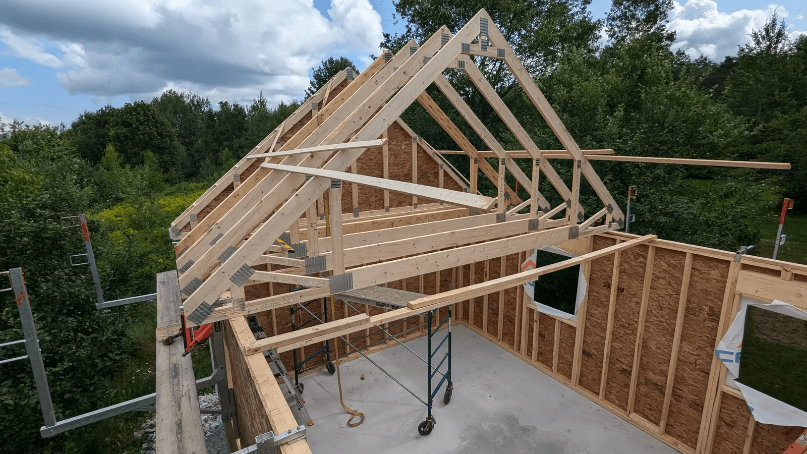 Charpente en bois d’une maison en construction avec fermes de toit, murs ossaturés, panneaux structuraux et échafaudage sur un chantier résidentiel
