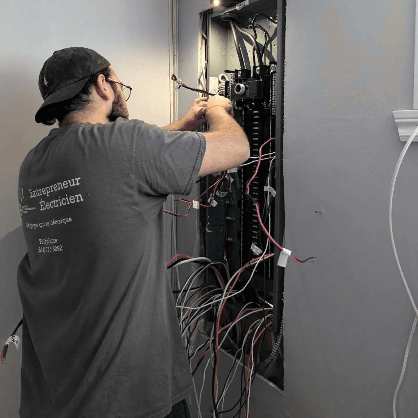 Un électricien effectuant des réparations sur un tableau électrique résidentiel avec des câbles apparents.