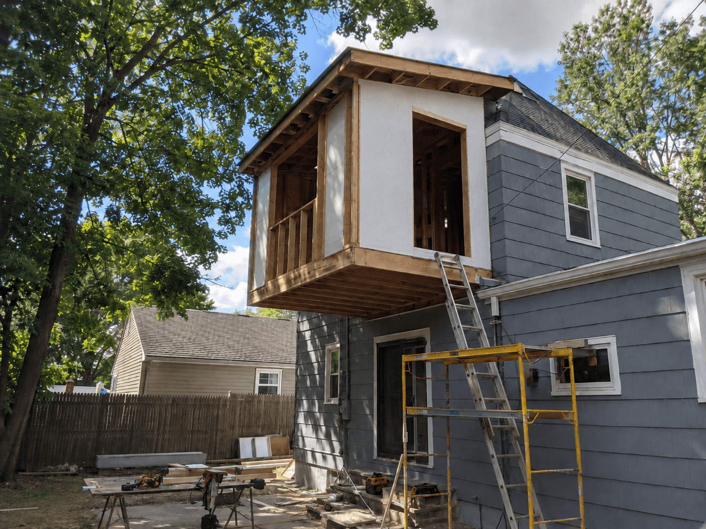 Agrandissement arrière en porte-à-faux au deuxième étage d’une maison, en cours de construction avec charpente en bois, panneaux structuraux, grandes ouvertures, échafaudage et échelle
