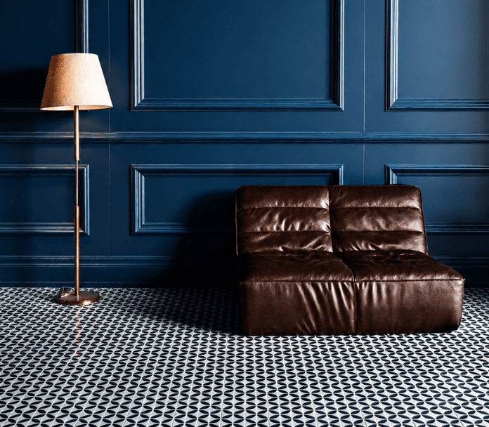 Salon élégant avec mur à panneaux bleu marine foncé, fauteuil en cuir brun, lampadaire et carrelage géométrique noir et blanc.