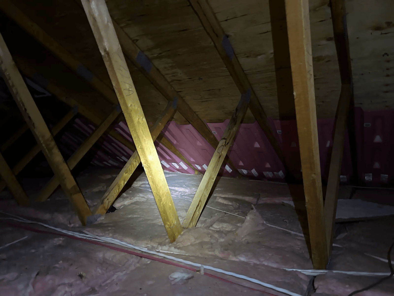 Grenier résidentiel avec charpente en bois, isolation en fibre entre les solives et inspection à la lampe de poche dans un espace de combles sombre