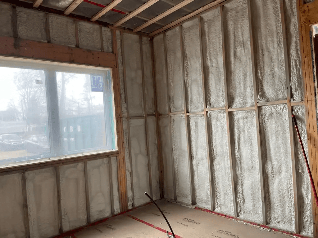 Mur intérieur en rénovation avec ossature en bois, isolation en mousse pulvérisée, fenêtre installée et préparation du plafond avant la pose du gypse
