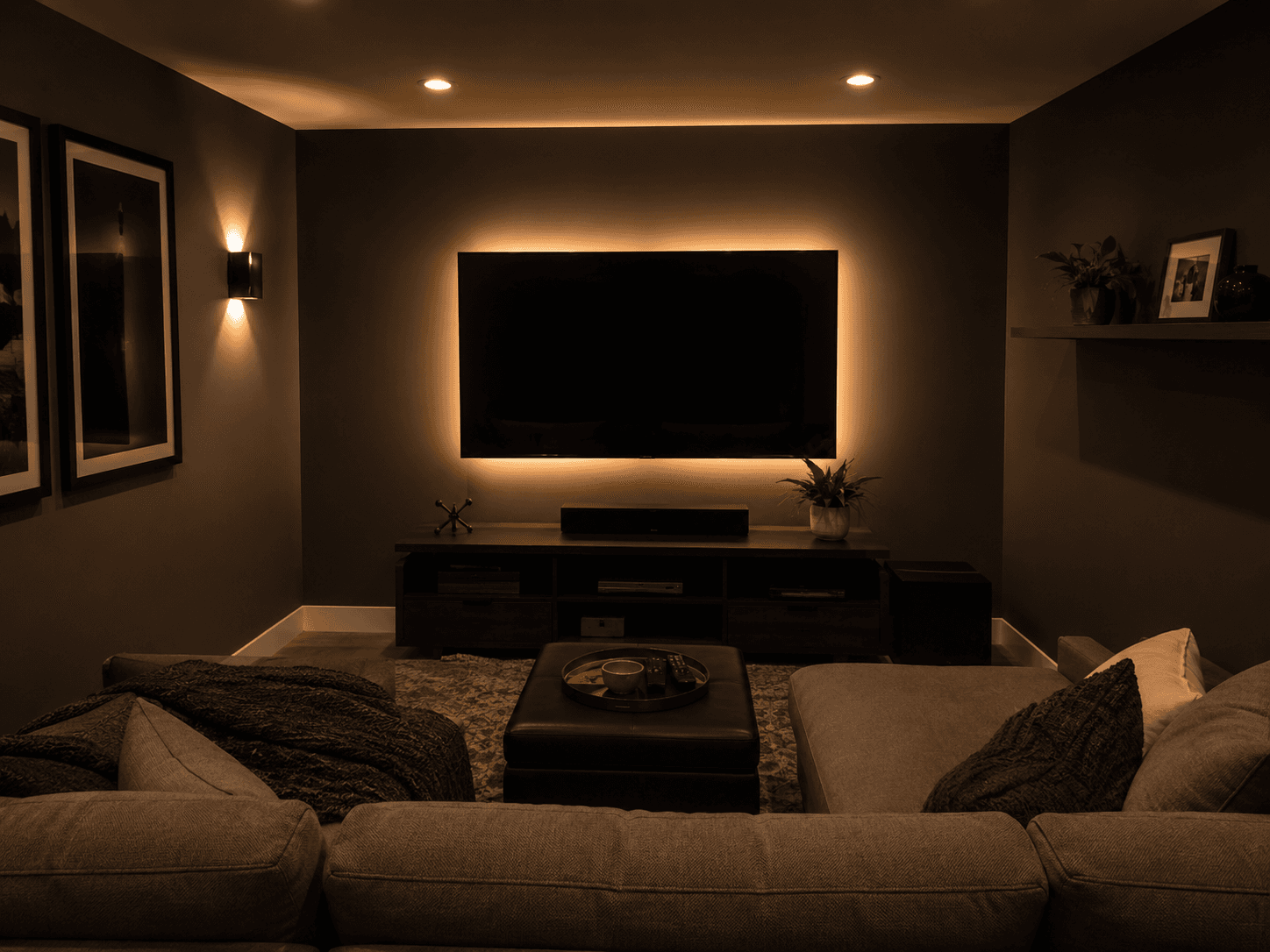 Petite salle multimédia avec grand téléviseur mural, éclairage d’accentuation derrière l’écran, canapé sectionnel et ambiance chaleureuse et tamisée.