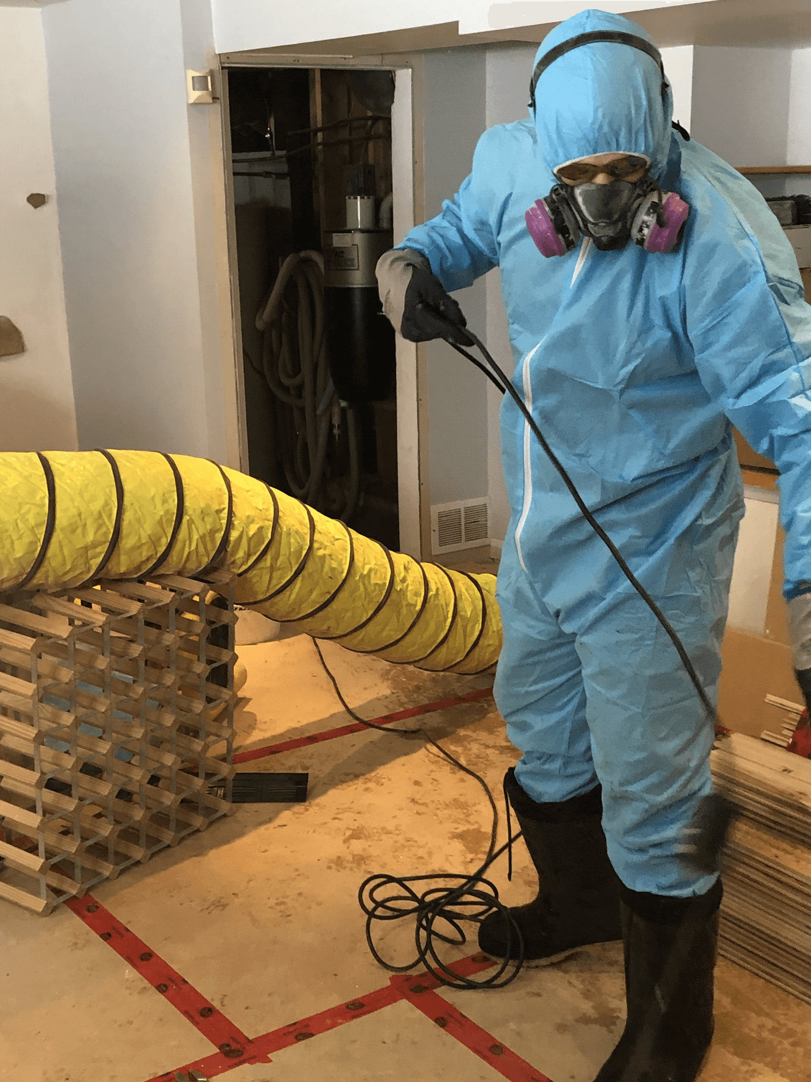 Technicien en décontamination portant une combinaison de protection bleue, un respirateur et des gants lors d’une intervention intérieure avec système de ventilation temporaire