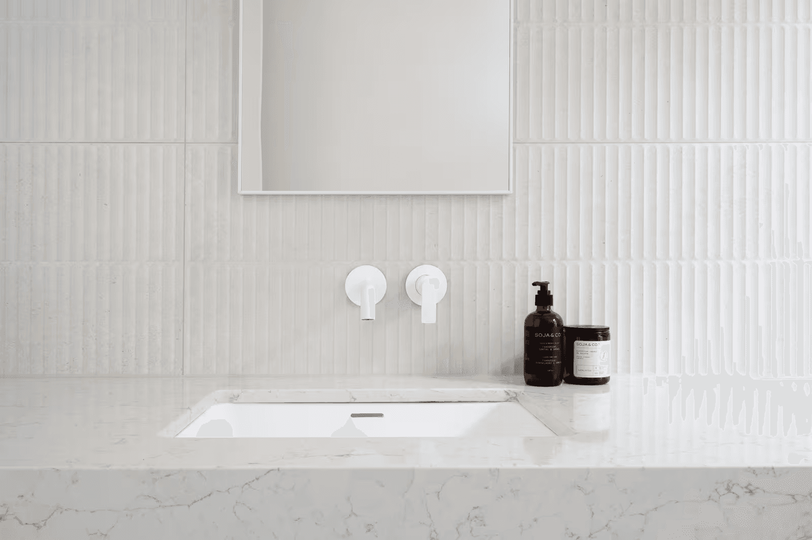 Lavabo moderne encastré en quartz avec robinetterie murale blanche et carrelage texturé dans une salle de bain minimaliste