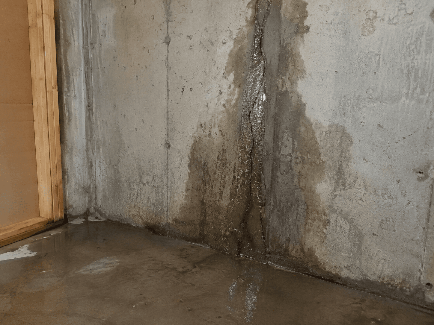 Mur de fondation en béton présentant une fissure verticale avec infiltration d’eau et traces d’humidité au sous-sol / Concrete foundation wall showing a vertical crack with water infiltration and visible moisture damage in a basement