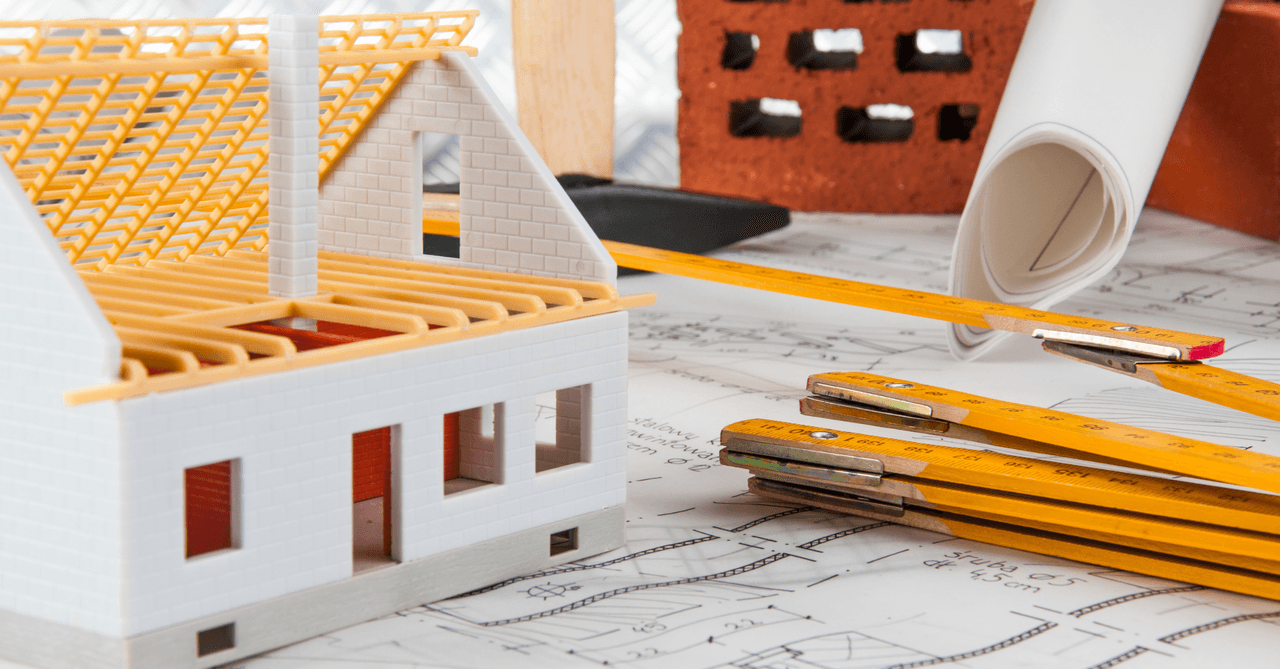 Maquette de maison blanche sur des plans d'architecte avec une règle jaune pliante et des briques en arrière-plan