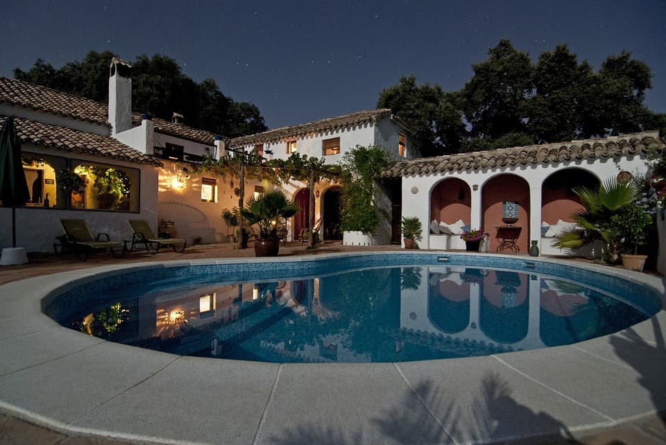 Cour arrière luxueuse avec piscine creusée éclairée la nuit au bord d'une villa de style méditerranéen.