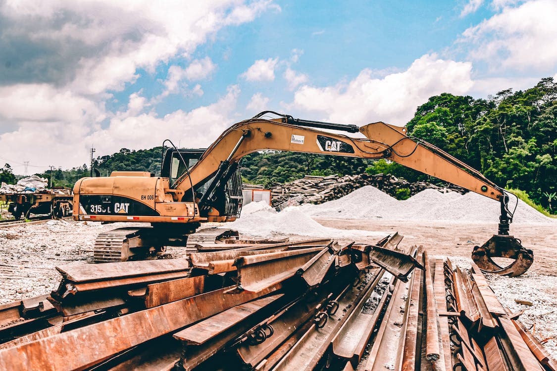 Excavatrice jaune CAT sur un chantier de construction avec des poutres en acier et des tas de gravier