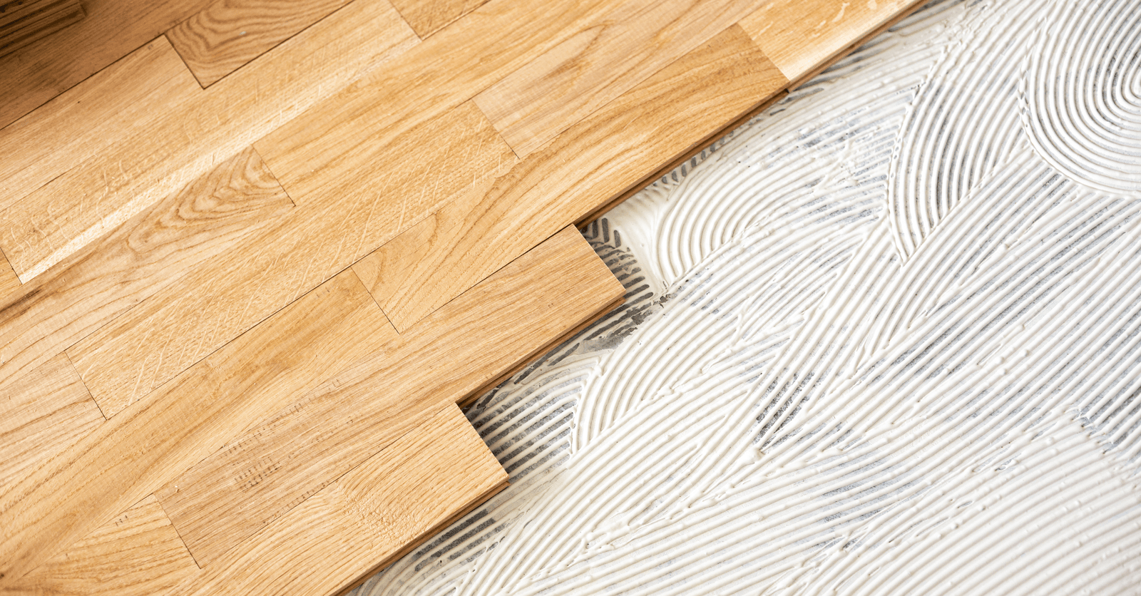 Pose de parquet en bois massif : lames de parquet en chêne clair étant collées sur une sous-couche adhésive
